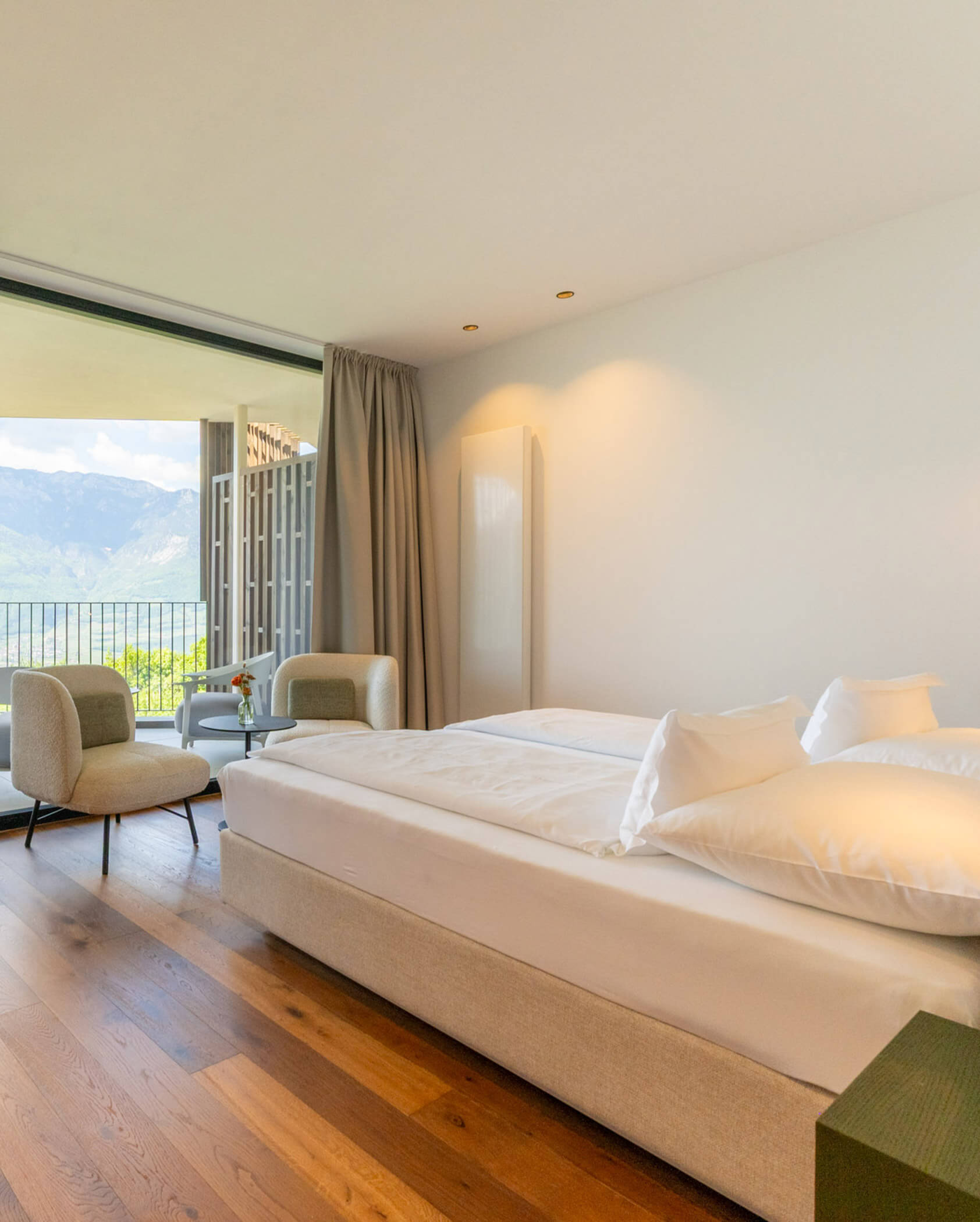 Una luminosa camera d'albergo con un grande letto, due sedie e un balcone con vista sulle montagne. - Hotel Tenz